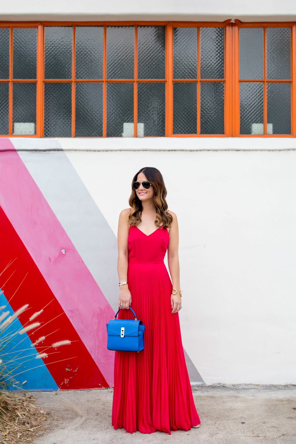 Jennifer Lake Style Charade in an ASOS pink pleated maxi dress, blue Henri Bendel Mini Uptown satchel, at a Free City striped wall in Los Angeles