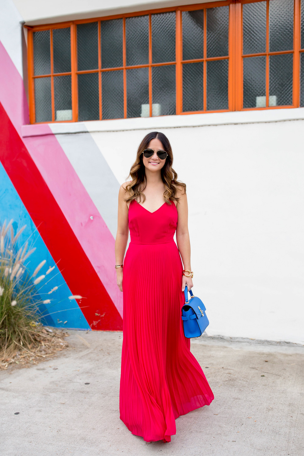 Jennifer Lake Style Charade in an ASOS pink pleated maxi dress, blue Henri Bendel Mini Uptown satchel, at a striped wall in Los Angeles