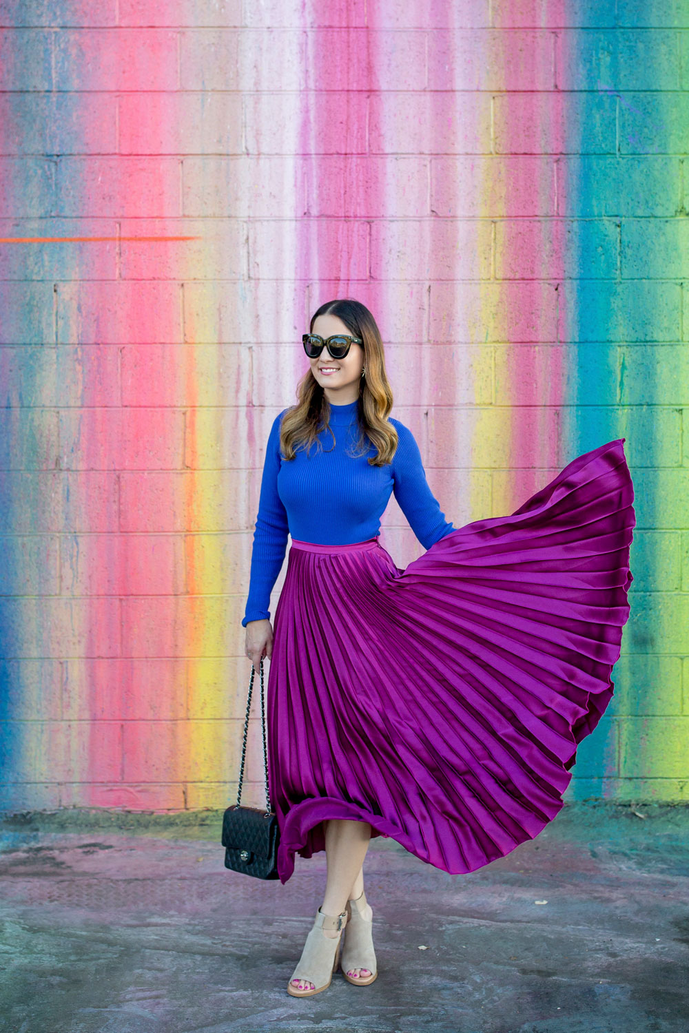 Jennifer Lake Style Charade flicking a ASOS purple pleated midi skirt, cobalt blue sweater bodysuit and Chanel quilted flap bag at a dripping paint wall in Los Angeles