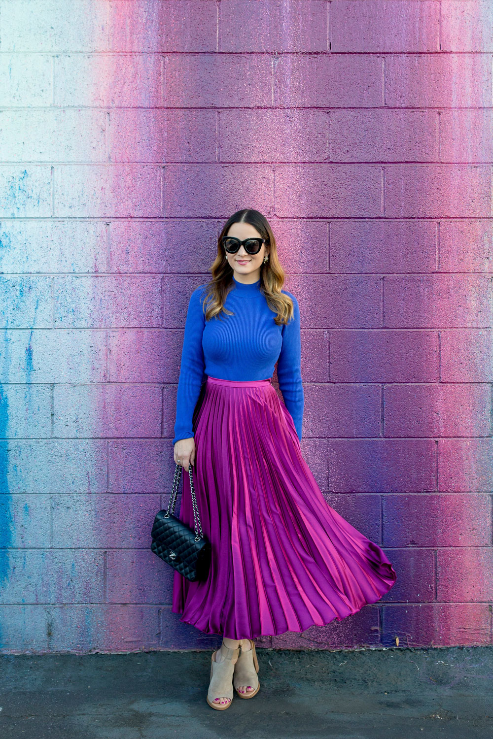 Jennifer Lake Style Charade in an ASOS purple pleated midi skirt, cobalt blue sweater bodysuit and Chanel quilted flap bag at a dripping paint wall in Los Angeles