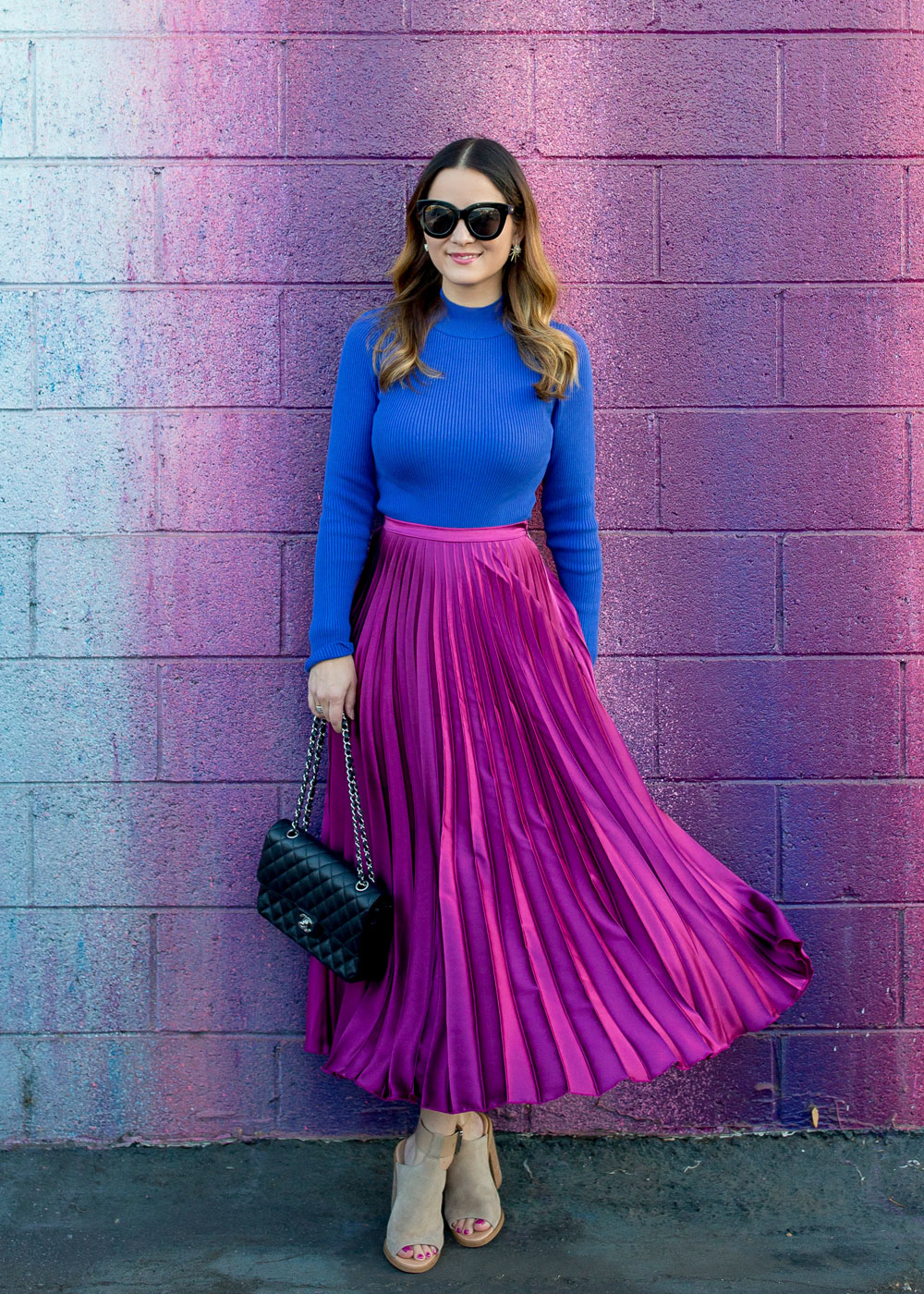 Jennifer Lake Style Charade in an ASOS purple pleated midi skirt, cobalt blue sweater bodysuit and Chanel quilted flap bag at a dripping paint wall in Los Angeles