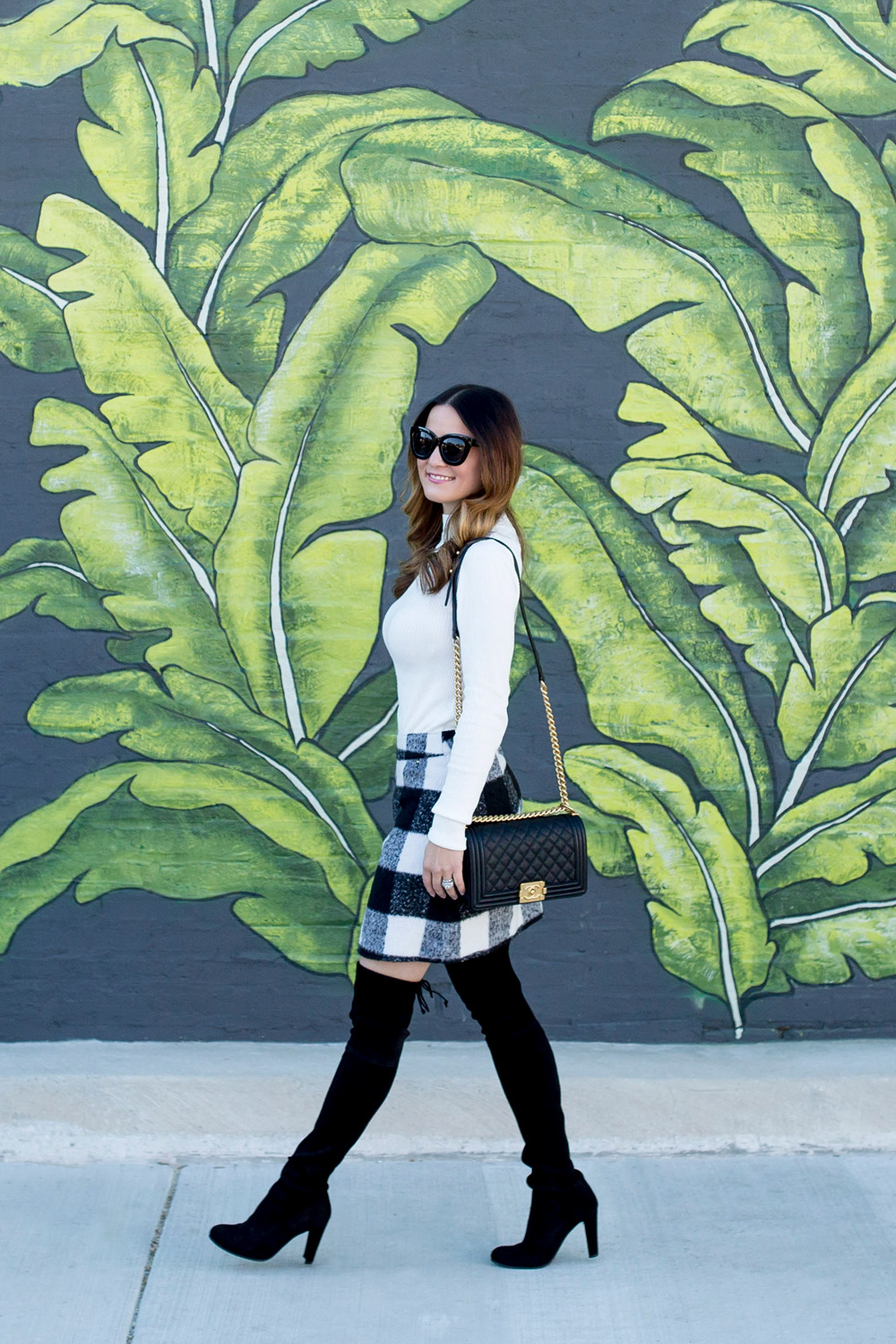 Jennifer Lake Style Charade in an ASOS black white check skirt, Chanel Boy Bag, and Stuart Weitzman Highland boots at a Chicago palm leaf mural