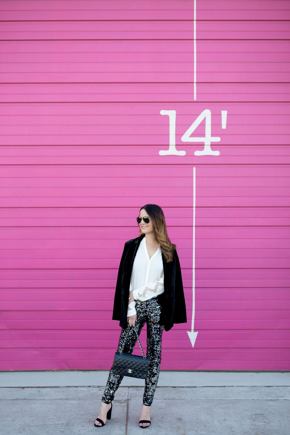 Jennifer Lake Style Charade in Express sequin leggings, black velvet blazer, ivory lace top, and a quilted Chanel flap bag in front of a Chicago pink wall