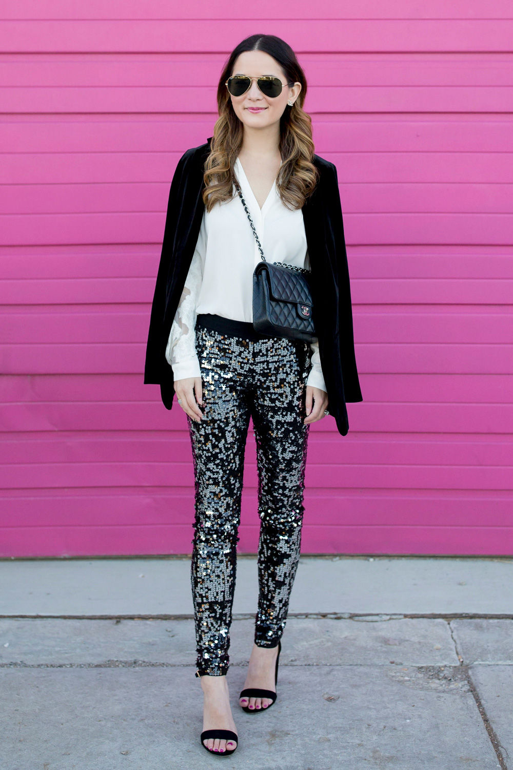 Jennifer Lake Style Charade in Express sequin leggings, black velvet blazer, ivory lace top, and a quilted Chanel flap bag in front of a Chicago pink wall