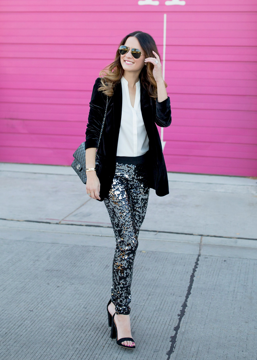 Jennifer Lake Style Charade in Express sequin leggings, black velvet blazer, ivory lace top, and a quilted Chanel flap bag in front of a Chicago pink wall