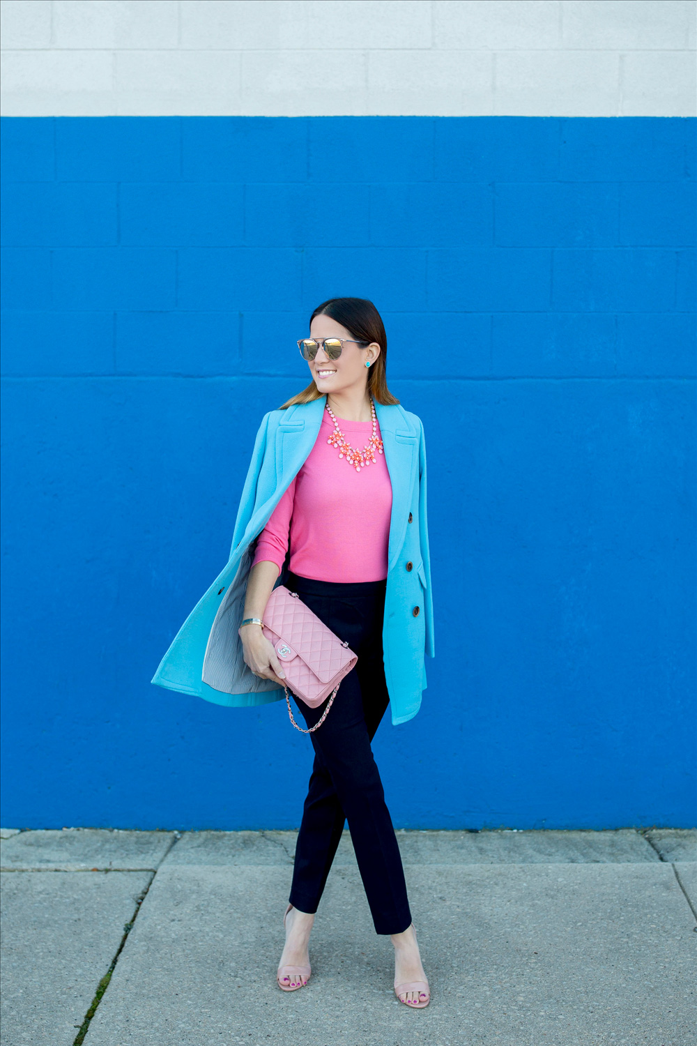 Jennifer Lake Style Charade in J Crew Nordstrom blue coat, pink cashmere sweater, pink Chanel quilted flap bag, and Steve Madden Carrson sandals at a blue wall in Chicago