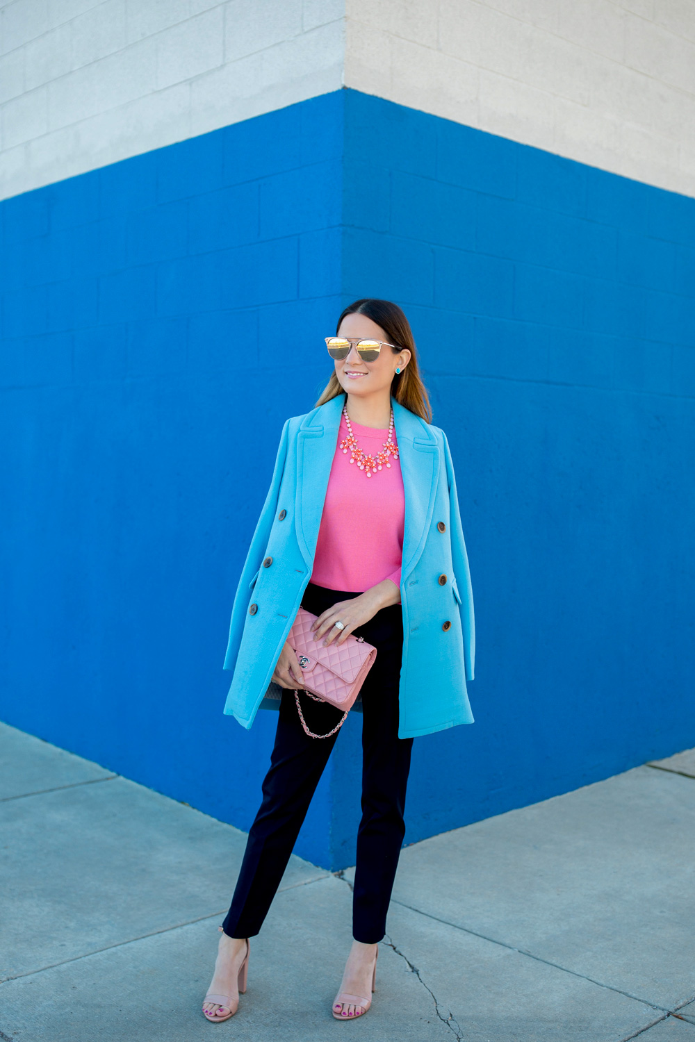 Jennifer Lake Style Charade in J Crew Nordstrom blue coat, pink cashmere sweater, pink Chanel quilted flap bag, and Steve Madden Carrson sandals at a blue wall in Chicago