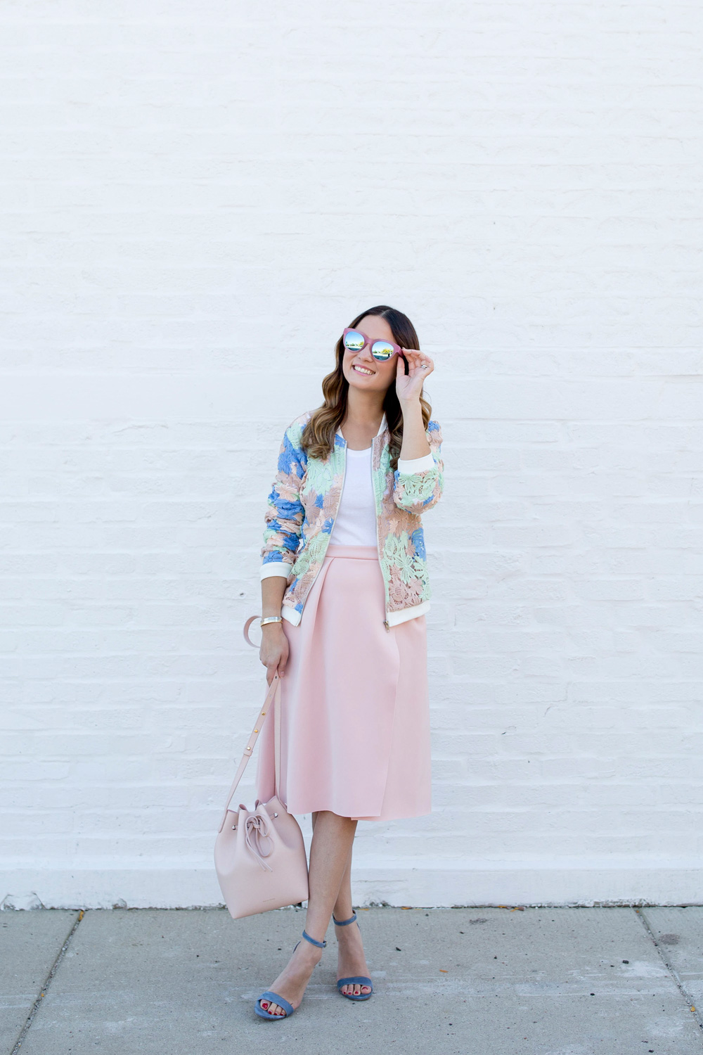 Jennifer Lake Style Charade in a pastel lace bomber jacket, pink skirt, pink Mansur Gavriel Bucket bag, and Packed Party Toms sunglasses
