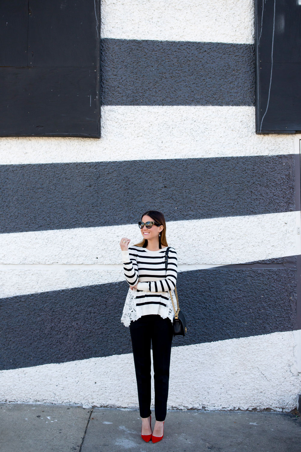Jennifer Lake Style Charade in a black and white stripe sweater with lace detail, a Chanel Boy Bag, and red pumps at a black and white wall in Chicago