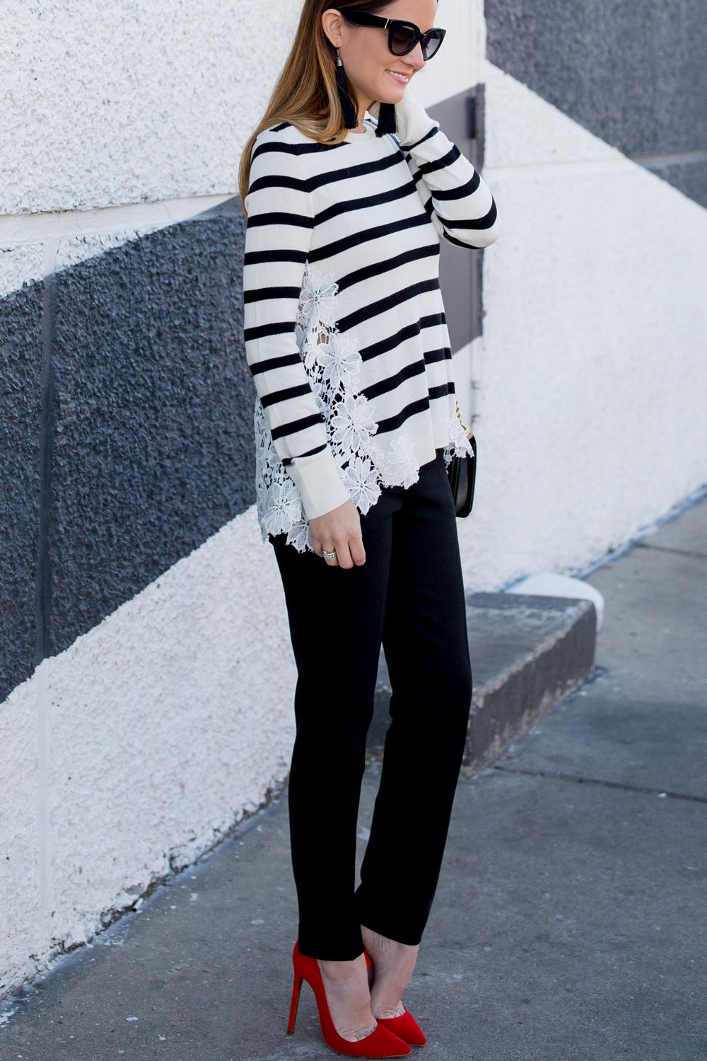 Jennifer Lake Style Charade in a black and white stripe sweater with lace detail, black tassel earrings, and red pumps at a black and white wall in Chicago