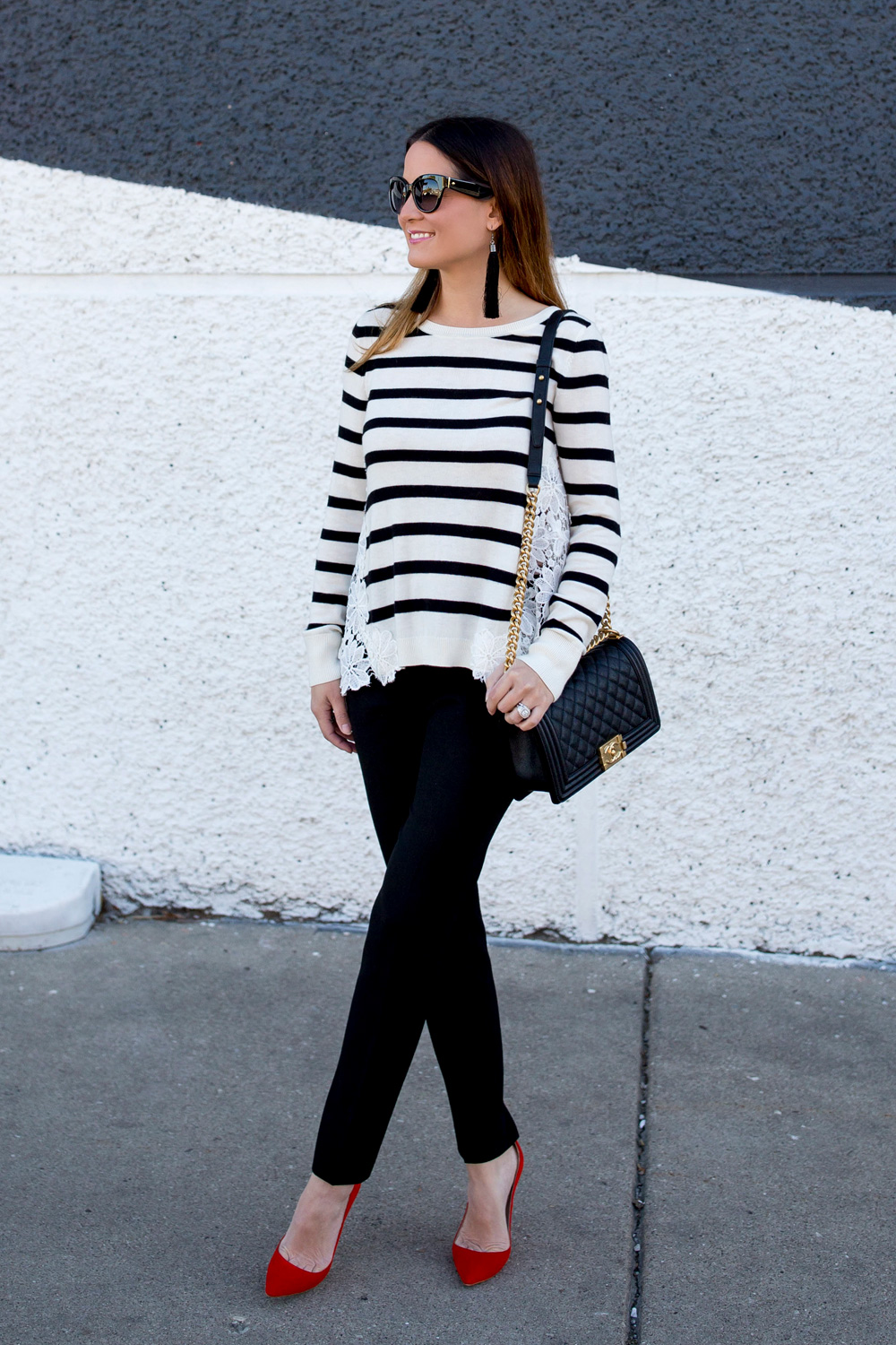 Jennifer Lake Style Charade in a black and white stripe sweater with lace detail, a black and gold Chanel Boy Bag and red pumps at a black and white wall in Chicago