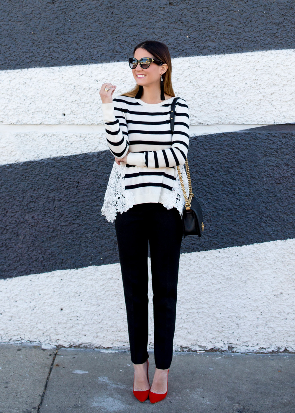 Jennifer Lake Style Charade in a black and white stripe sweater with lace detail, a Chanel Boy Bag, and red pumps at a black and white striped wall in Chicago